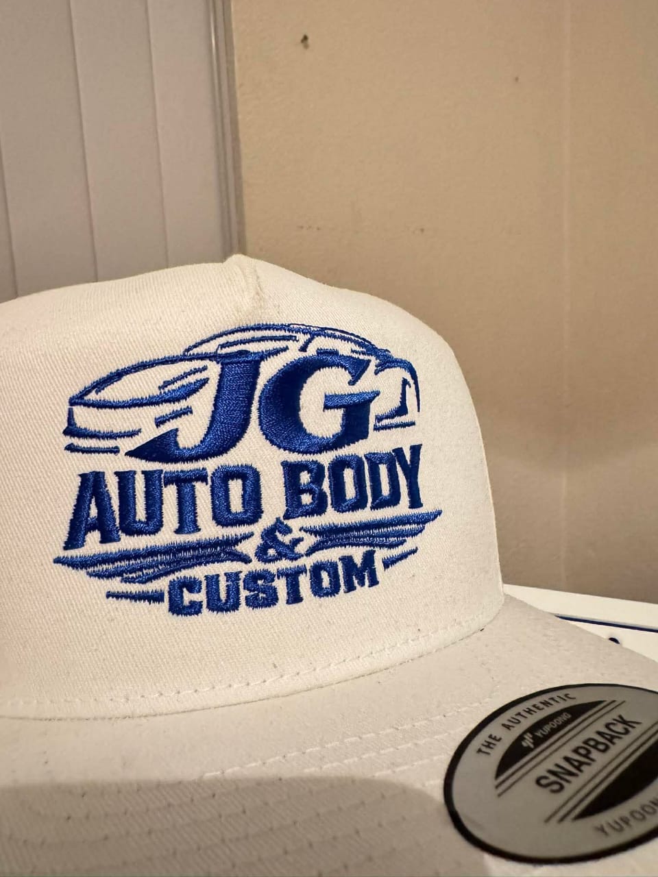 Custom JG Auto Body and Custom logo embroidery on white snapback cap with blue thread