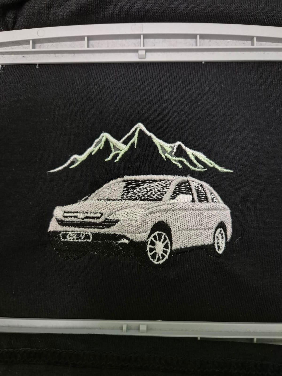 Car and mountain embroidery sample showing detailed stitch work on black fabric.