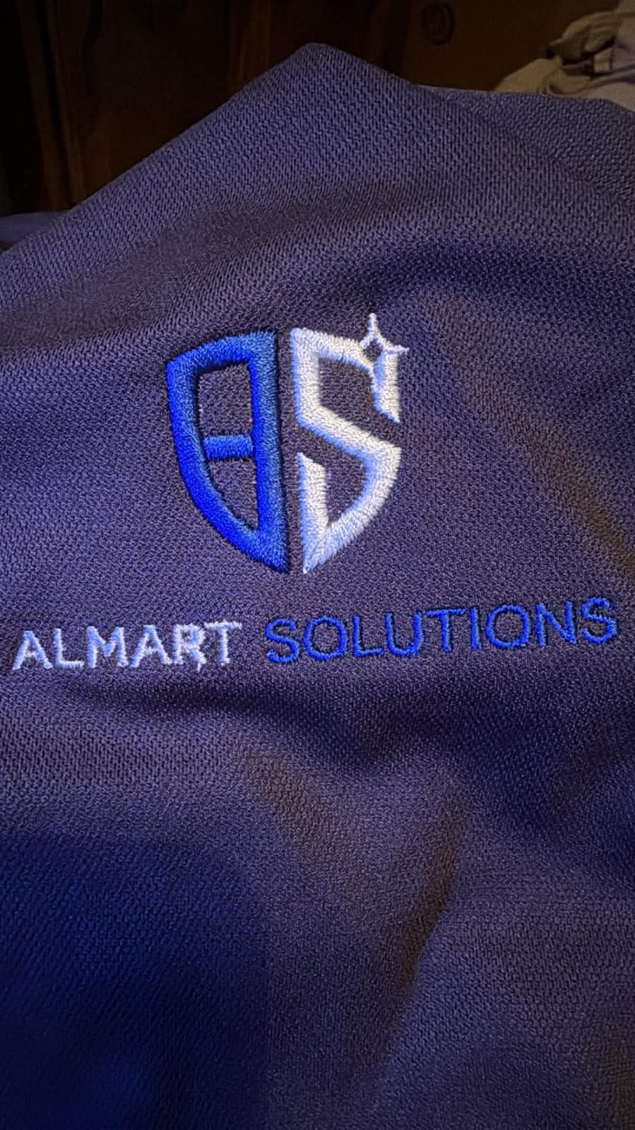 Almart Solutions embroidered business logo sample on dark fabric.
