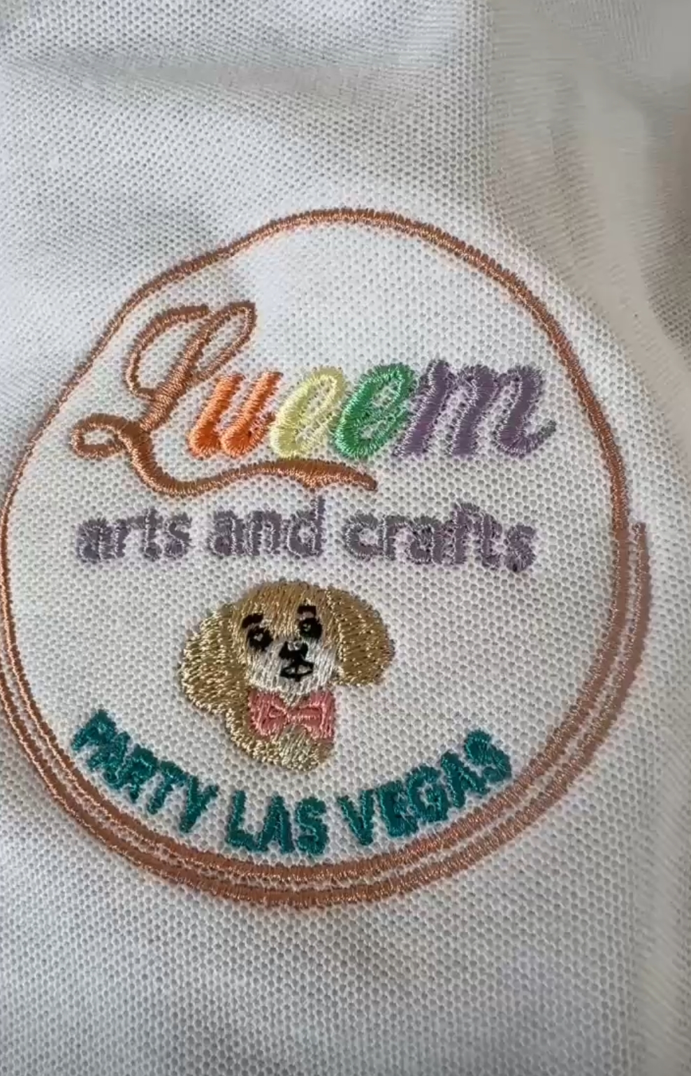 Queen Arts and Crafts embroidered badge sample with colorful text and dog illustration.